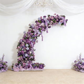 Floral arch display with purple roses and blossoms against a white backdrop.