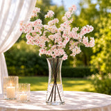 Pink blossom arrangement in glass vase with candles on outdoor table