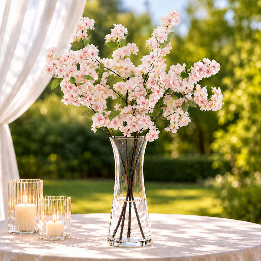 Pink blossom arrangement in glass vase with candles on outdoor table