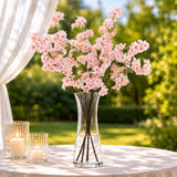Pink cherry blossom arrangement in glass vase with candles on outdoor table