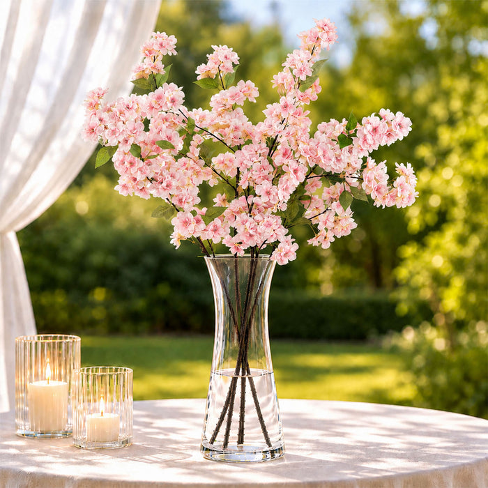 Pink cherry blossom arrangement in glass vase with candles on outdoor table