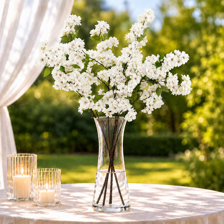 White floral arrangement in glass vase with candles on outdoor table