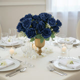 Elegant navy blue rose centerpiece in a gold vase on a dining table setting.