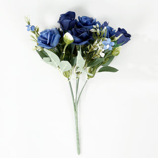 <p style="margin-left:0px;"><strong>Beauty Redefined with Navy Blue Real Touch Artificial Rose Bouquet</strong></p><p style="margin-left:0px;">Choosing our Navy Blue Real Touch Artificial Silk Rose Bridal Bouquet will bring a sense of elegance and class to any setting right away. These <a href="https://tableclothsfactory.com/collections/artificial-flowers"><u>artificial flowers</u></a> are crafted with precision to provide a realistic feel of real roses, showcasing a rich navy blue shade that adds a touch of regal sophistication. Whether you're getting ready for a wedding, a special event, or simply looking to enhance your home decor, these <strong>rose bouquets</strong> offer a classic allure that will leave a lasting impression.</p><p style="margin-left:0px;">These artificial rose arrangements promise a realistic sensation that replicates the delicate petals of actual roses. This feature goes beyond appearance, as it also involves the tactile experience that makes guests question whether these roses are real or fake. Imagine the surprise and amazement on your guests' faces when they discover that the lovely tabletop centerpiece, which looks like it was just picked, is actually a fake arrangement designed to last years. This flral bouquet is perfect for people who appreciate the beauty of nature but want the convenience and long-lasting quality of artificial flowers.</p><p style="margin-left:0px;">The deep navy blue color of these silk roses can complement various color palettes and decor themes. These roses appear beautiful whether they are paired with white table linens or vibrant decorations. They can easily mix in with any style of decor, whether it's classic or modern. Use them to create beautiful bridal bouquets, striking <strong>tabletop centerpieces</strong>, or elegant home decor displays. There are endless possibilities with this stunning artificial flower display.</p>