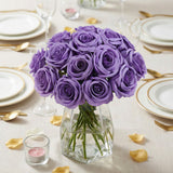 Purple roses bouquet in a clear vase on a dinner table setting.