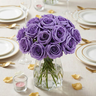 Purple roses bouquet in a clear vase on a dinner table setting.