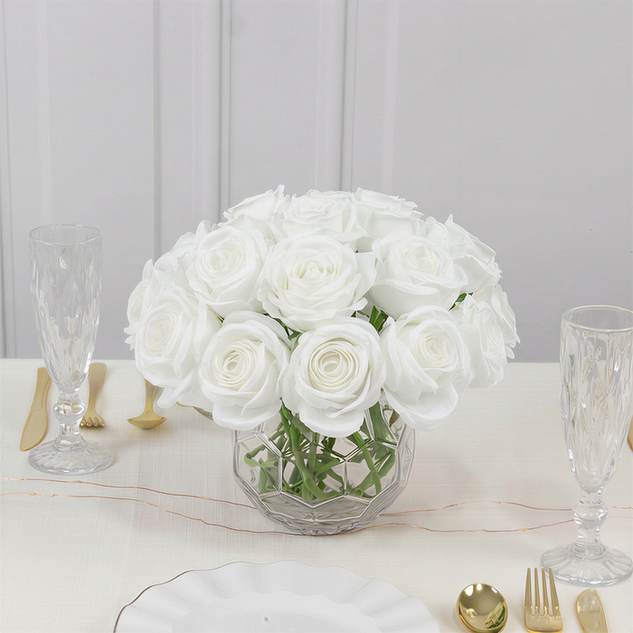 White roses in a glass vase on a dining table setting.