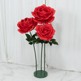 Red artificial roses in a green stand against a white backdrop.