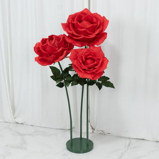 Red artificial roses in a green stand against a white backdrop.
