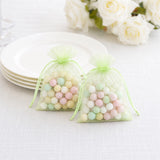 Pastel candy in green organza gift bags on a white table setting