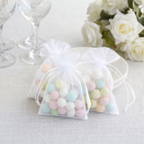 Pastel candy favor bags on a white table with roses and glassware
