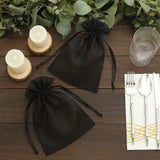 Black organza gift bags on a wooden table with candles and tableware.