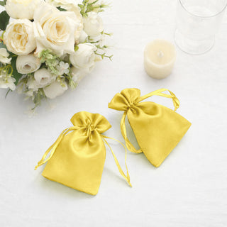 Yellow satin drawstring bags on a table with flowers and a candle.