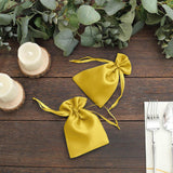 Yellow satin drawstring bags on a wooden table with greenery and candles.