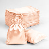 Satin drawstring bags in peach color, stacked and one bag displayed.