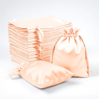 Stack of peach satin drawstring bags on a white background.