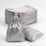 Stack of silver satin drawstring bags on a white background.