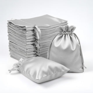 Silver satin drawstring bags stacked and arranged on a white backdrop.