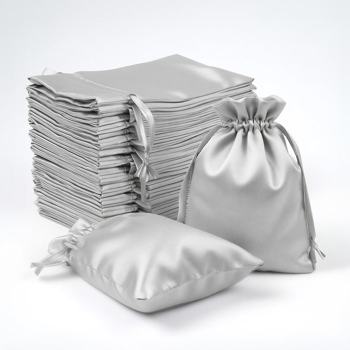 Silver satin drawstring bags stacked and arranged on a white backdrop.