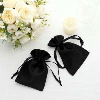 Two elegant black satin drawstring bags on a table with white flowers.