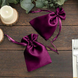 Purple satin drawstring bags on a wooden table with greenery and candles.