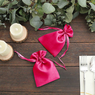 Pink satin drawstring bags on a rustic wooden table with greenery and candles.