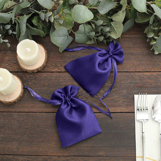 Purple satin drawstring bags on a rustic wooden table with candles and greenery.