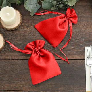Red satin drawstring gift bags on a wooden table.
