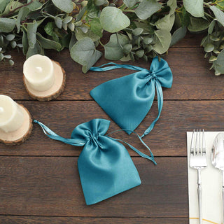 Teal satin gift bags with ribbon ties, styled with greenery and candles.