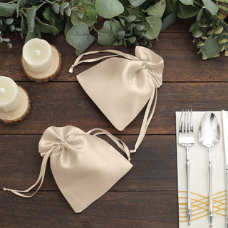 Beige satin drawstring bags on a rustic wooden table with greenery and candles.
