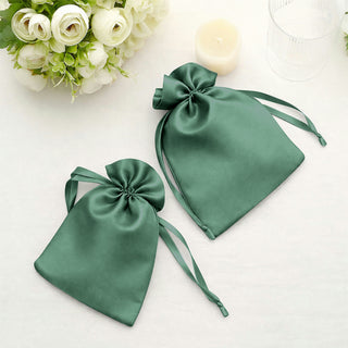 Green satin drawstring bags on a soft surface with white flowers and a candle.