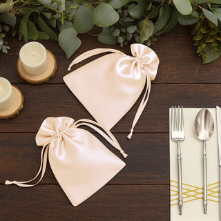 Two elegant satin favor bags in blush pink with ribbon ties on a wooden table.