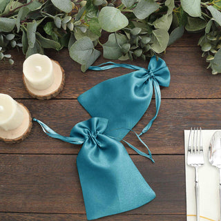 Teal satin gift bags with ribbon ties, styled with candles and greenery.