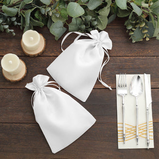 White satin drawstring gift bags with elegant decor on a rustic wooden table.