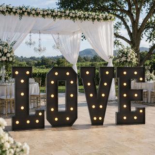 Large illuminated LOVE sign at outdoor wedding reception under floral canopy