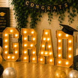 Gold “GRAD” marquee lights with graduation decor and cap banner for celebration.