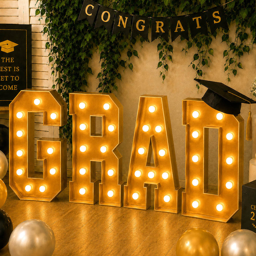 Gold “GRAD” marquee lights with graduation decor and cap banner for celebration.