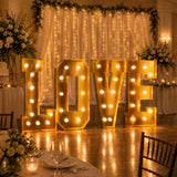 Gold illuminated LOVE letters at a wedding reception backdrop with fairy lights