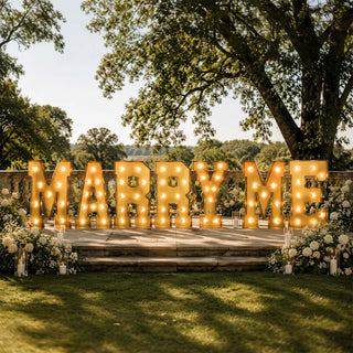 Marquee “Marry Me” proposal sign with flowers outdoors in a garden venue