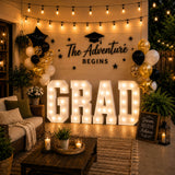 Graduation party backdrop with lit GRAD sign, balloons, and string lights