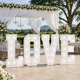Outdoor wedding decor with illuminated LOVE sign under floral canopy