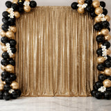 Gold sequin backdrop with black and gold balloon arch for events or photography.