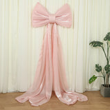 Large pink satin bow with flowing ribbons against a backdrop.