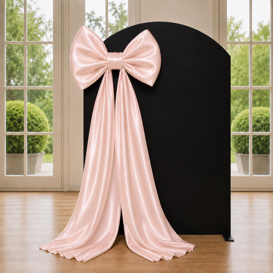 Pink satin bow and draped ribbon on black backdrop near window