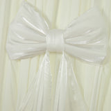 White satin bow on pleated fabric backdrop.