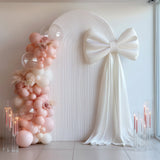 Elegant white backdrop with a large bow and pastel balloon arrangement.