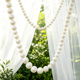 White pearl garland draped between sheer curtains in a garden setting