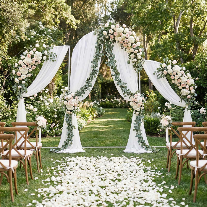 Elegant outdoor wedding arch with white drapes, greenery, and blush floral arrangements
