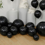 Black balloons in various sizes arranged on a wooden floor with white decorations.