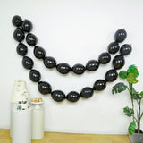 Black balloons arranged in a decorative garland against a plain wall.